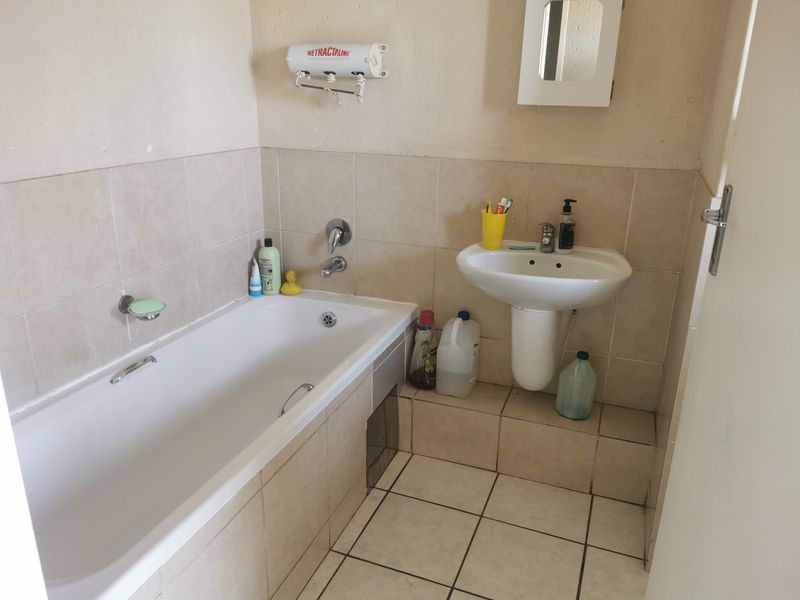 A compact bathroom featuring a standard bathtub, pedestal basin, and tiled finishes, requiring cosmetic updates to improve its overall condition and appeal.