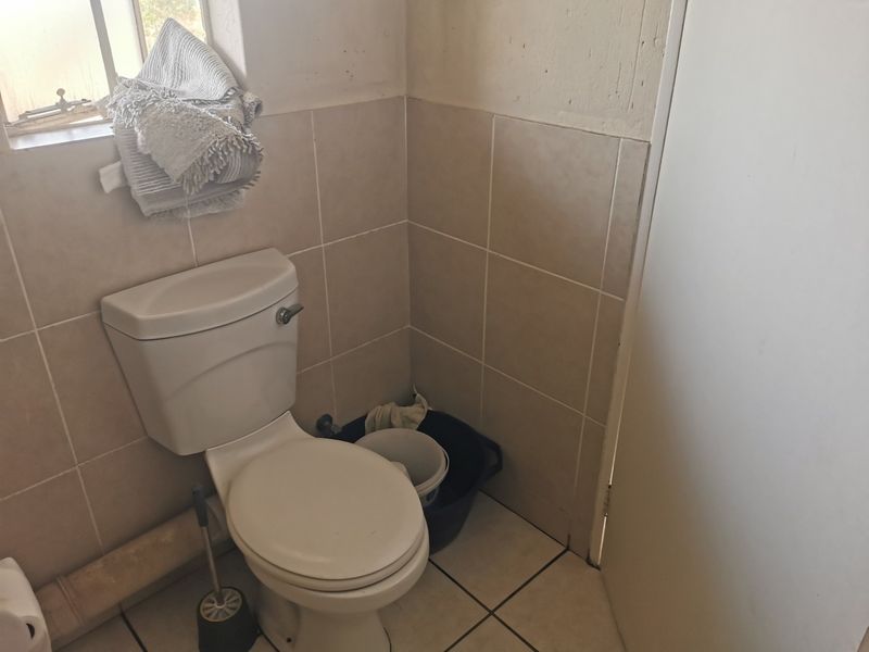 A compact bathroom featuring a standard toilet, tiled flooring, and tiled wall accents, requiring minor cosmetic updates to improve its overall appearance.