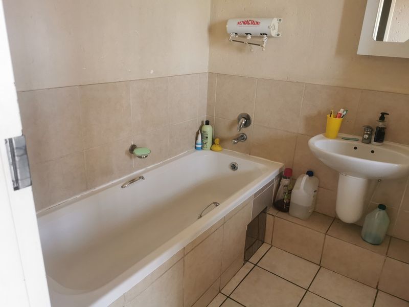 A functional bathroom featuring a standard bathtub, pedestal basin, and wall-mounted retractable clothesline, finished with neutral ceramic wall and floor tiles.