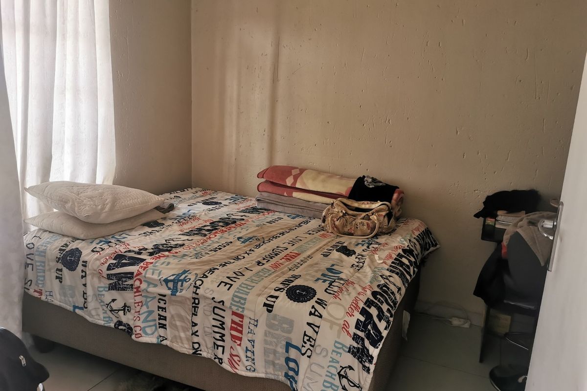 A compact bedroom featuring tiled flooring and a window with curtain rails, requiring minor wall repairs and cosmetic updates.