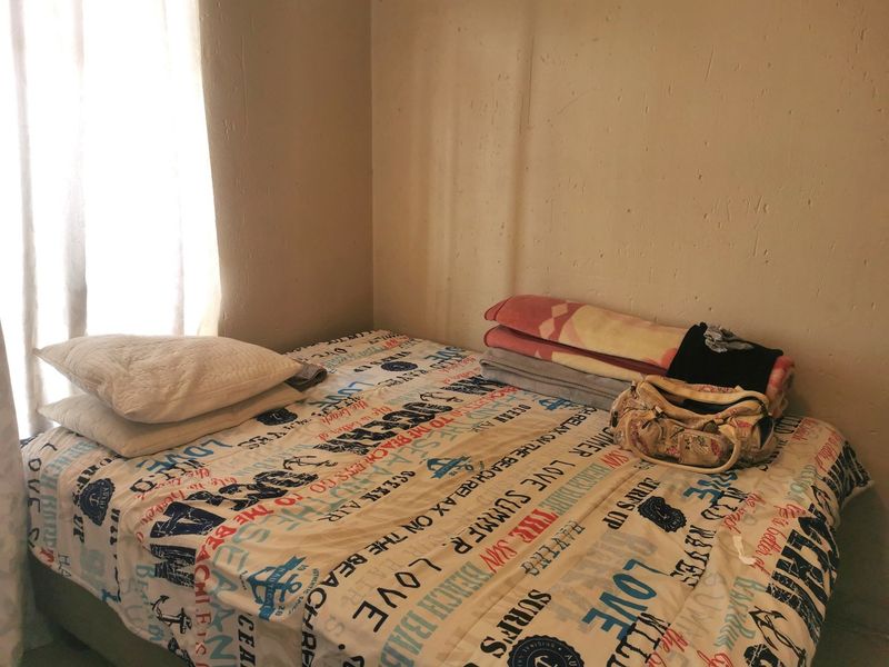 A compact bedroom space featuring plain walls and natural light from a side window.