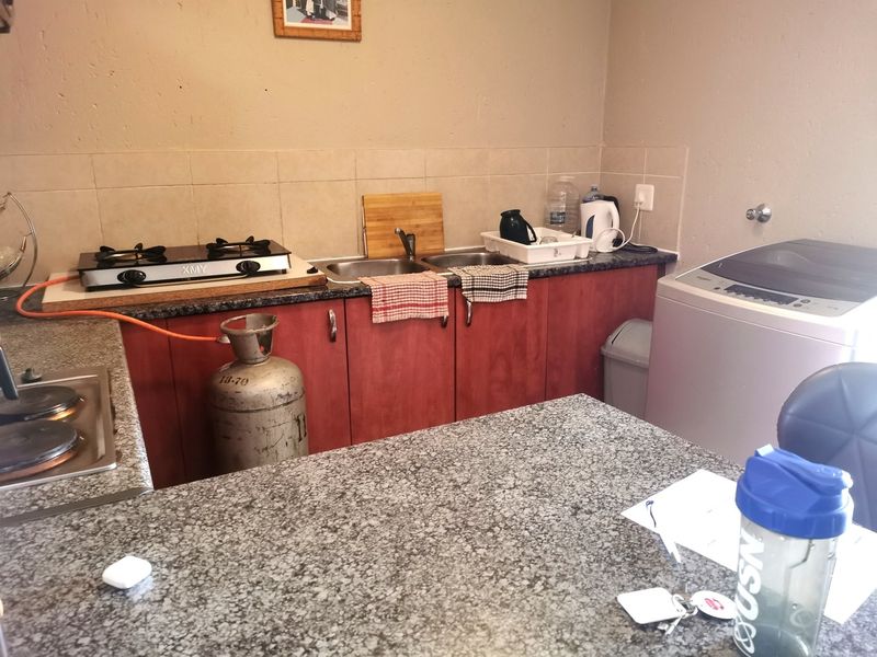 Compact kitchen featuring granite countertops, a double sink, built-in cabinetry, and a gas hob, requiring minor updates to improve functionality and aesthetic appeal.