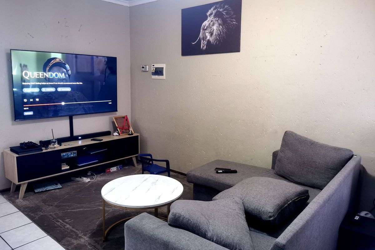 A living room featuring tiled flooring and a wall-mounted electrical distribution board, with visible wear on the wall surfaces.