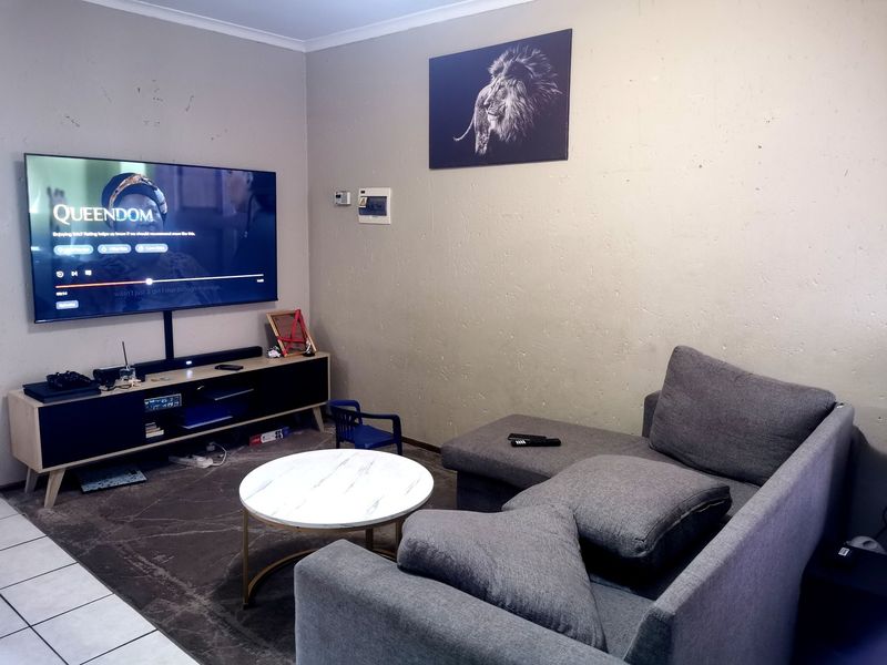 A living room featuring tiled flooring and a wall-mounted electrical distribution board, with visible wear on the wall surfaces.