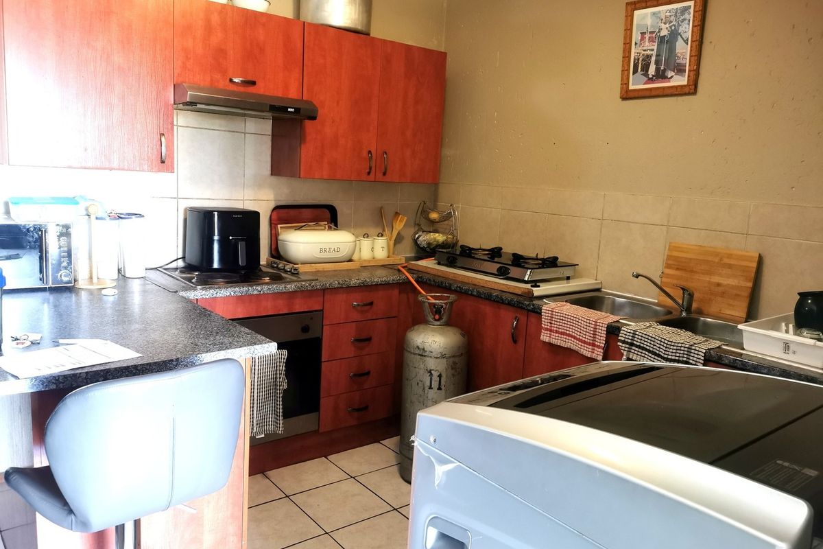 A functional kitchen featuring laminate cabinetry, tiled backsplash, built-in oven, extractor fan, and stainless steel sink with ceramic tile flooring.