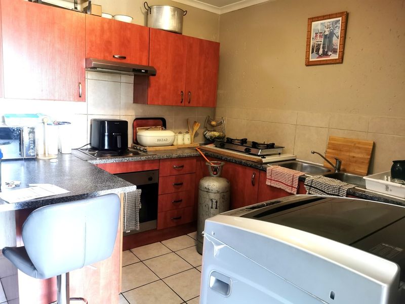 A functional kitchen featuring laminate cabinetry, tiled backsplash, built-in oven, extractor fan, and stainless steel sink with ceramic tile flooring.