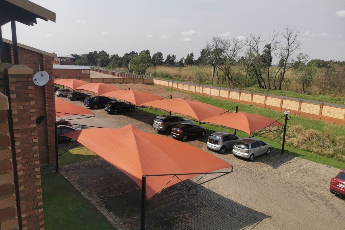 Elevated view of the apartment complex parking area featuring multiple shade cloth carports and paved driveway surfaces.