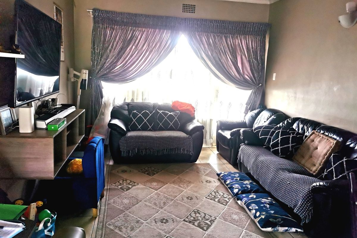 A comfortable living room featuring tiled flooring, neutral wall tones, and a large window with curtains, providing a functional space for relaxation.