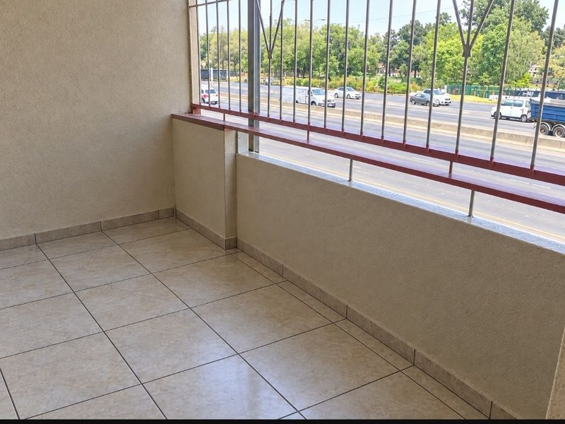 A clean, tiled balcony featuring metal security bars and an open view of the adjacent road.