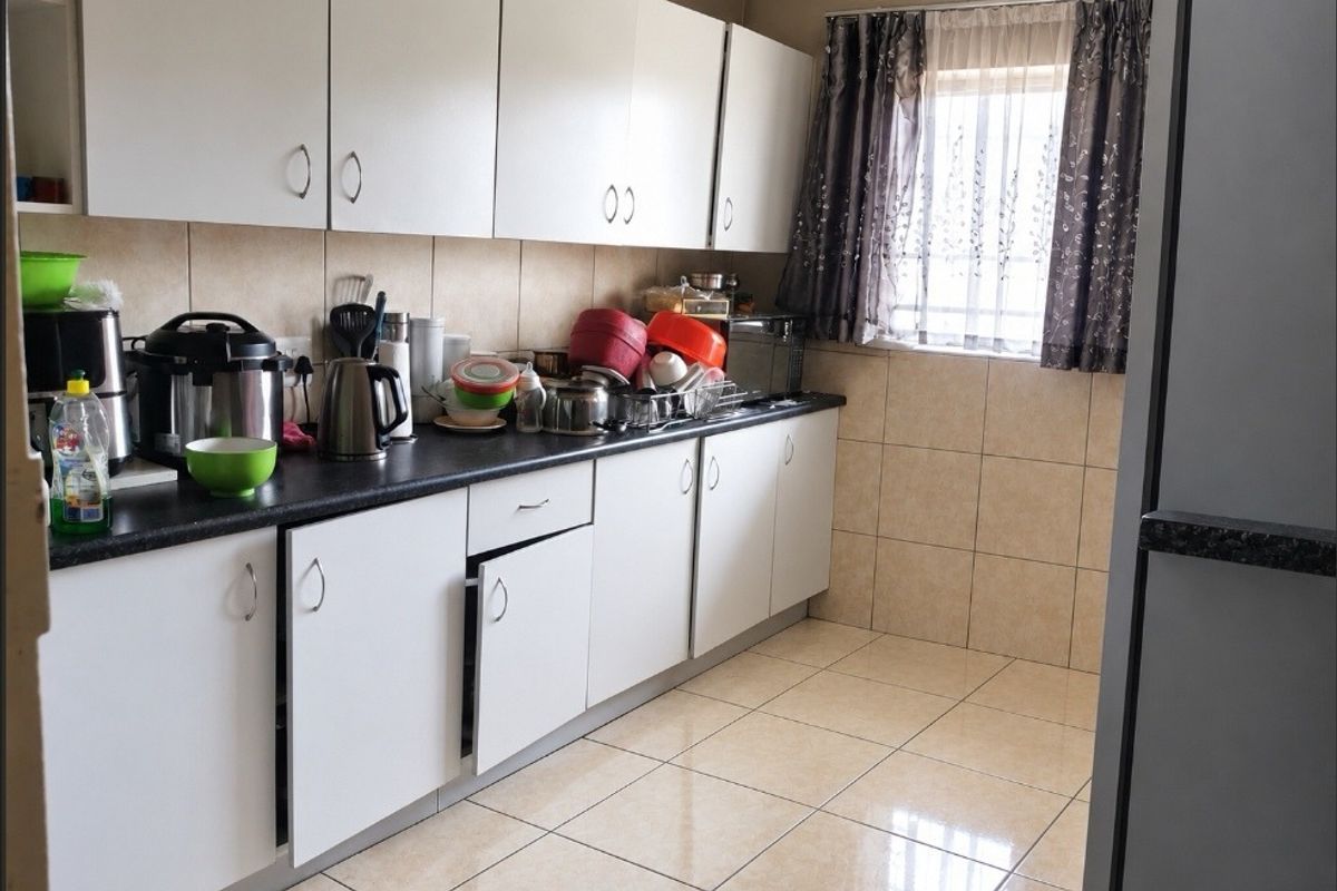 A functional kitchen featuring white cabinetry, dark laminate countertops, and neutral ceramic tiling throughout the floor and splashback areas.