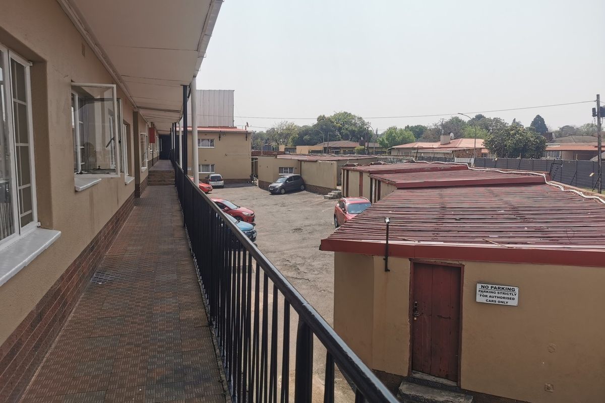An exterior view from an apartment walkway overlooking the rear parking area and garage structures.