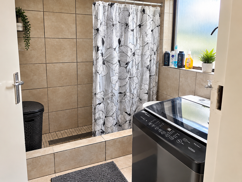 A functional laundry area featuring tiled walls and flooring, a built-in shower enclosure, and dedicated plumbing connections for laundry appliances.