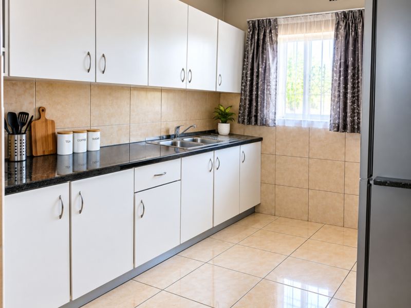A clean and functional kitchen featuring white cabinetry, dark granite countertops, tiled backsplash, and tiled flooring with a window providing natural light.