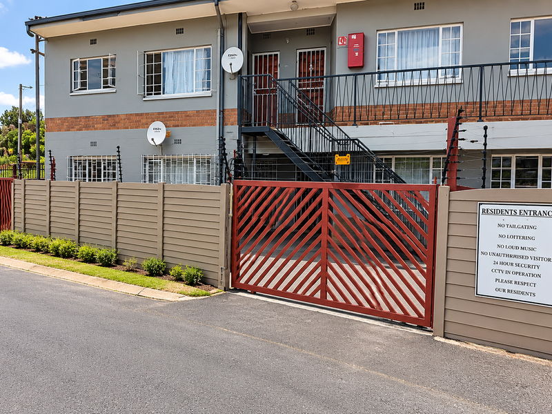 Front exterior view of an apartment complex featuring a secure gated entrance, electric fencing, and external metal staircase access to upper units.