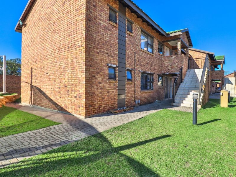 Rear view of a face brick apartment building featuring a paved walkway, landscaped lawn, and an external staircase leading to upper levels.