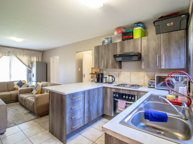Open-plan kitchen and living area featuring modern laminate cabinetry, built-in oven, electric hob, and tiled flooring throughout the space.