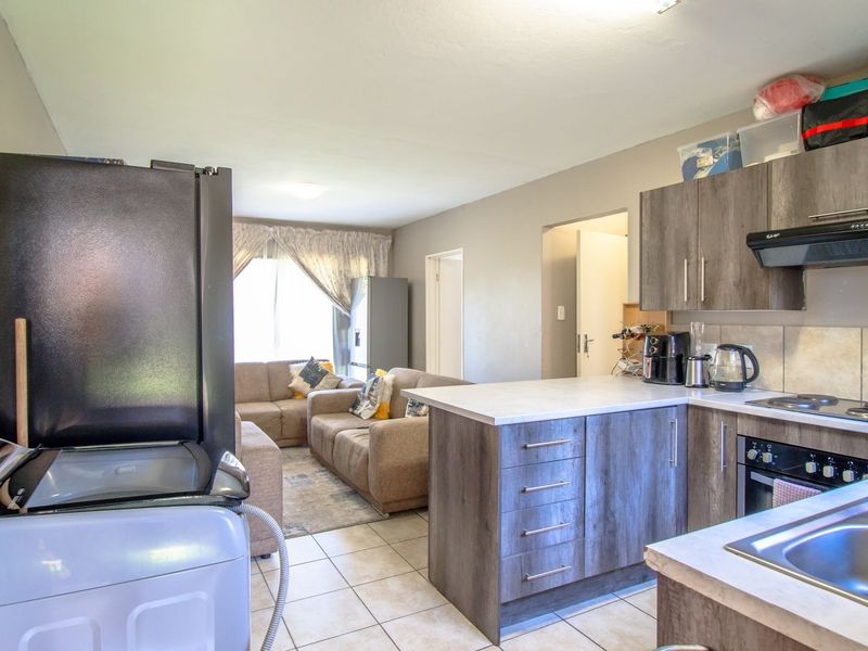 Open-plan living area featuring a functional kitchen with wood-look cabinetry, integrated appliances, and tiled flooring, seamlessly connecting to the adjacent lounge space.