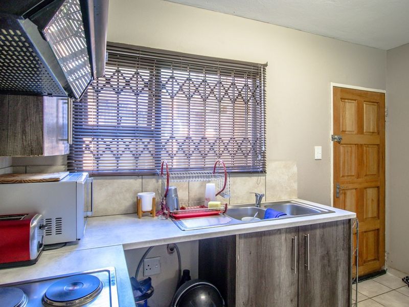A functional kitchen featuring built-in cabinetry, a stainless steel sink, a hob with an extractor fan, and a window with security bars.