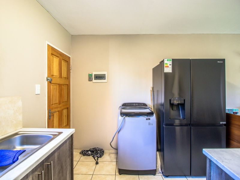 A functional laundry area featuring tiled flooring, a stainless steel sink, and direct access via a timber door.