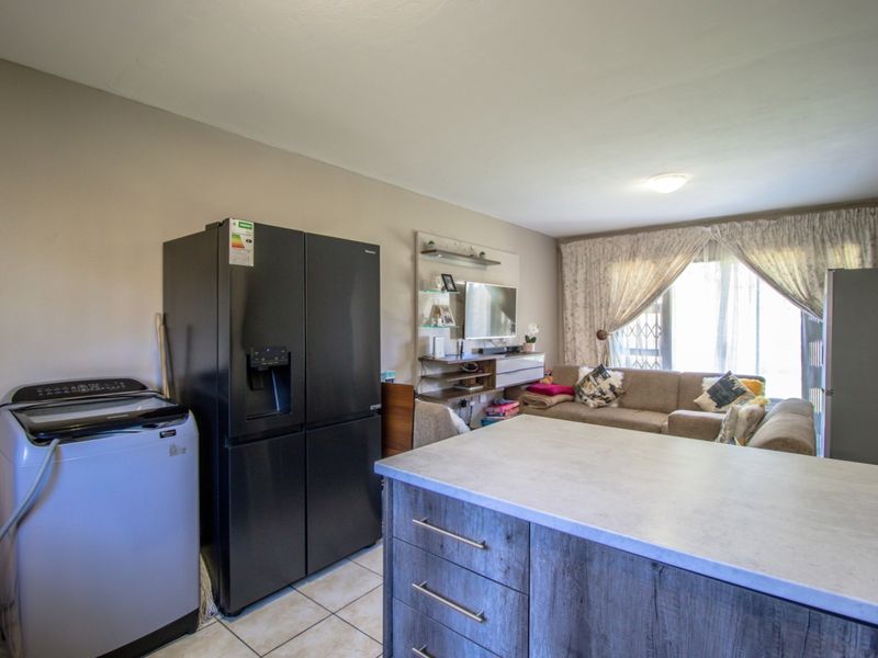 Open-plan living area featuring a kitchen island with stone-look countertop, tiled flooring, and direct access to the patio through a security gate.