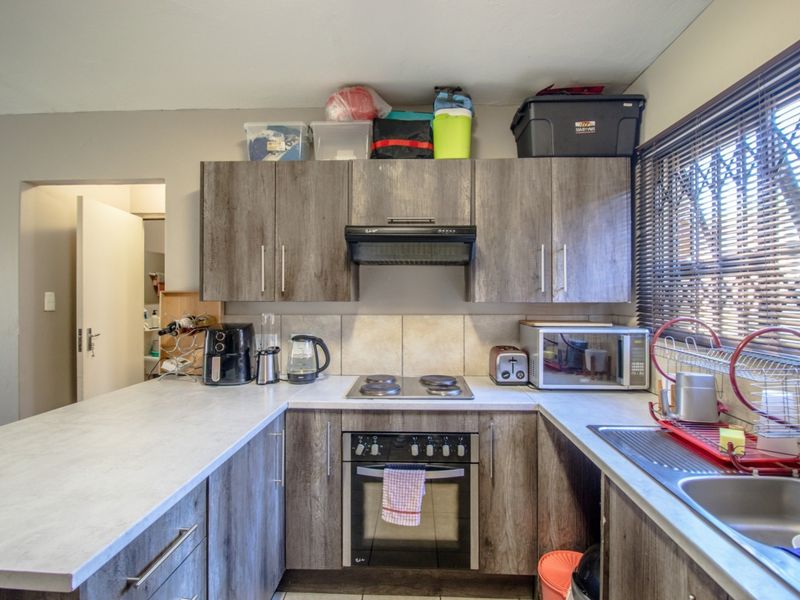 Functional kitchen featuring wood-look cabinetry, laminate countertops, built-in oven and hob, and a stainless steel sink with a window view.