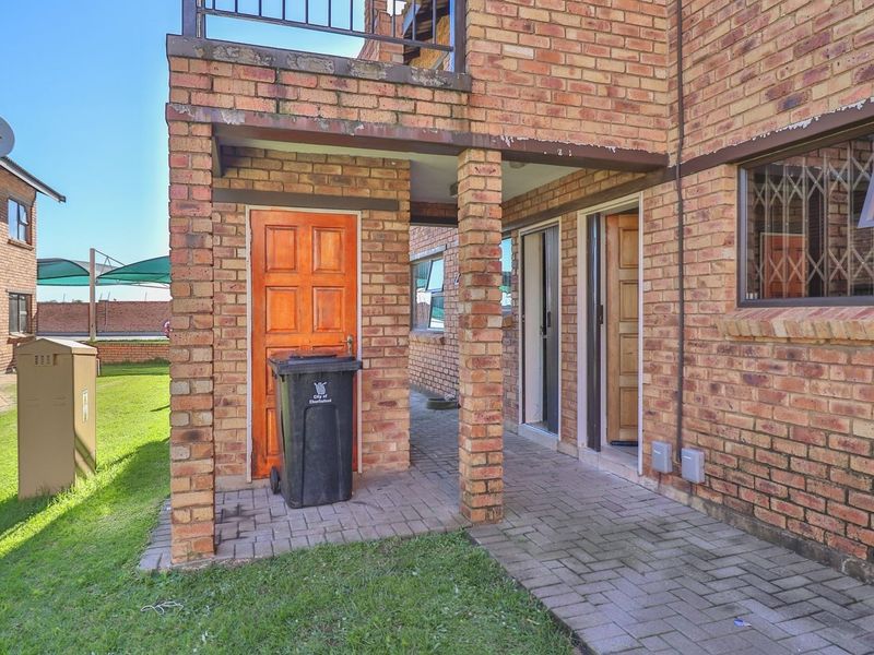 Rear exterior view of the apartment featuring a brick facade, paved patio area, and secure access points with timber doors and aluminium window frames.