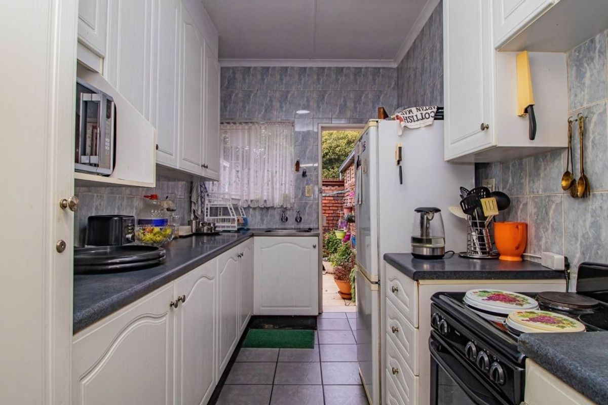 A functional galley-style kitchen featuring white cabinetry, dark laminate countertops, tiled backsplash, and direct access to an outdoor area.