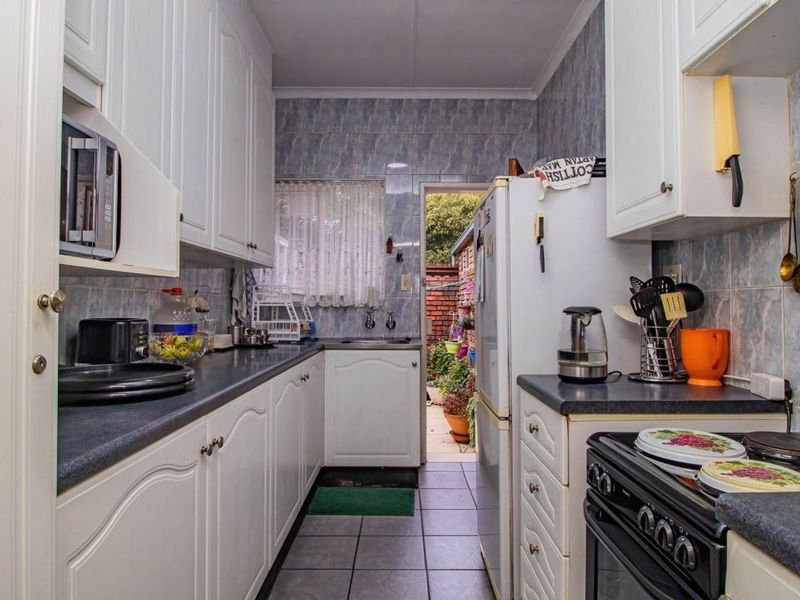 A functional galley-style kitchen featuring white cabinetry, dark laminate countertops, tiled backsplash, and direct access to an outdoor area.