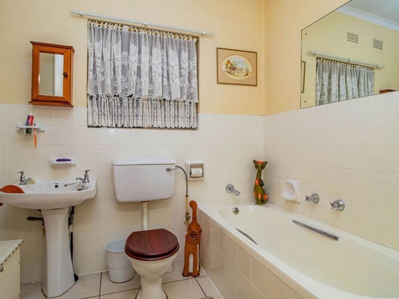 A functional bathroom featuring a pedestal basin, toilet, and bathtub with classic wall tiling and a large mirror.