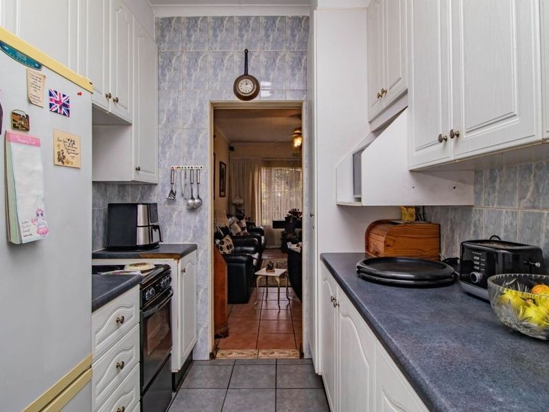 A functional galley-style kitchen featuring white cabinetry, dark laminate countertops, and tiled finishes, providing a practical workspace with direct access to the living area.