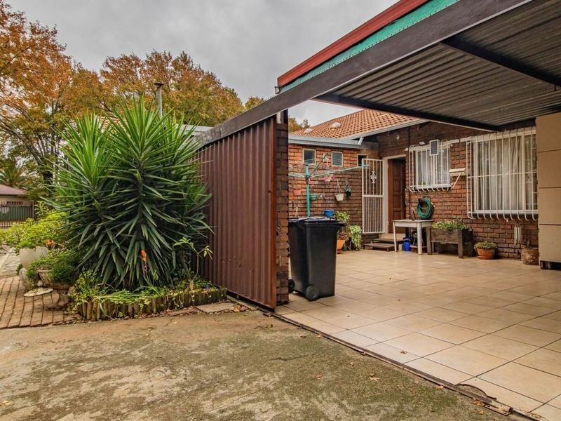 Front exterior view of the townhouse featuring a tiled carport, brick facade, and a paved entrance area with security features.