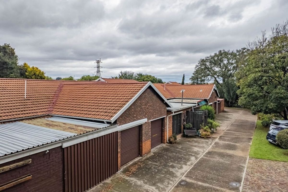 Aerial view of a townhouse complex featuring brick facades, terracotta tiled roofs, and a shared concrete driveway with multiple garage access points.
