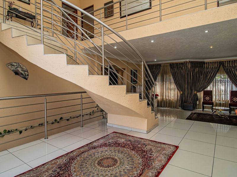 Spacious double-volume entrance hall featuring a prominent staircase with stainless steel balustrades, tiled flooring, and an open mezzanine landing.