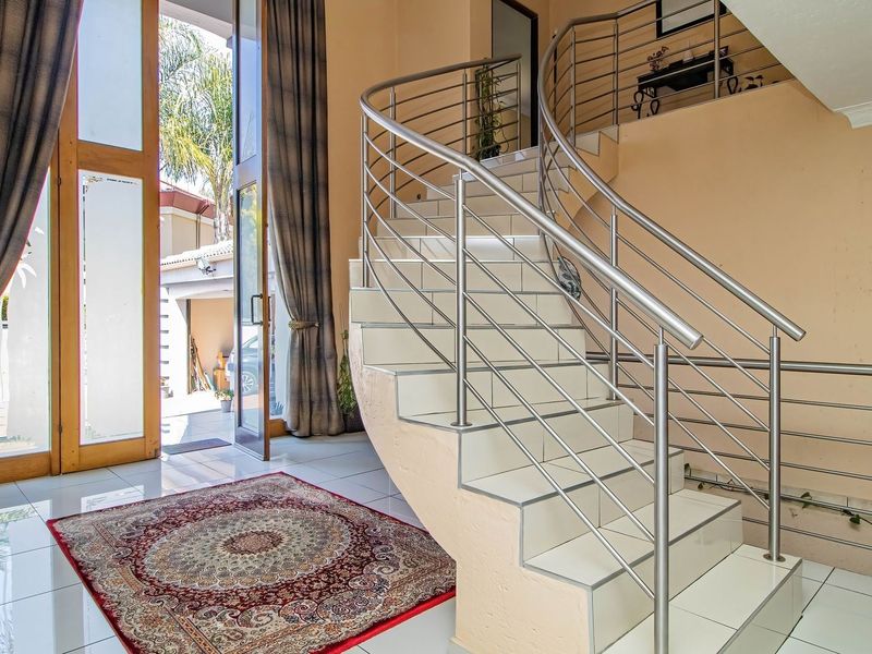 Spacious entrance hall featuring a prominent curved staircase with stainless steel balustrades and polished tiled flooring, leading to a bright, open entryway.