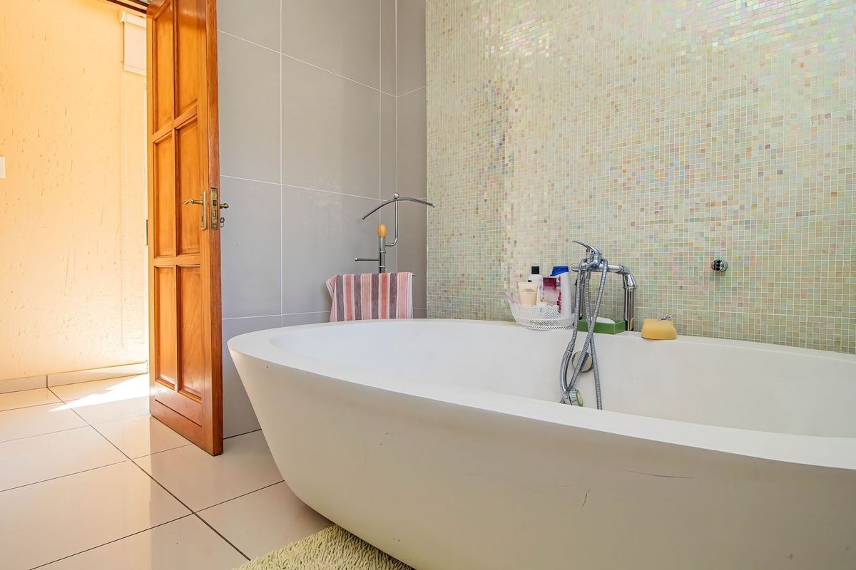 A bathroom featuring a modern freestanding bathtub set against a decorative mosaic tile feature wall with neutral ceramic floor tiles.