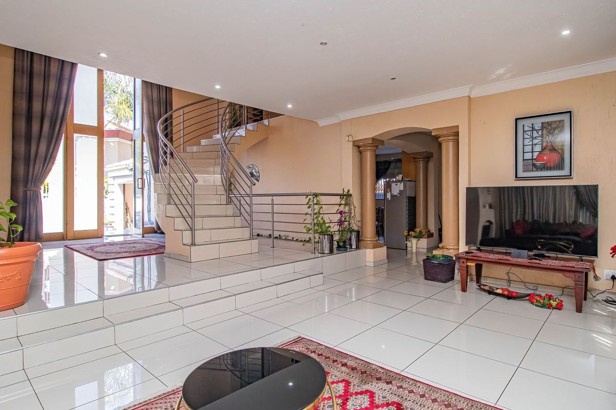 Spacious living area featuring large format floor tiles, a prominent curved staircase with stainless steel balustrades, and direct access to the outdoor area.