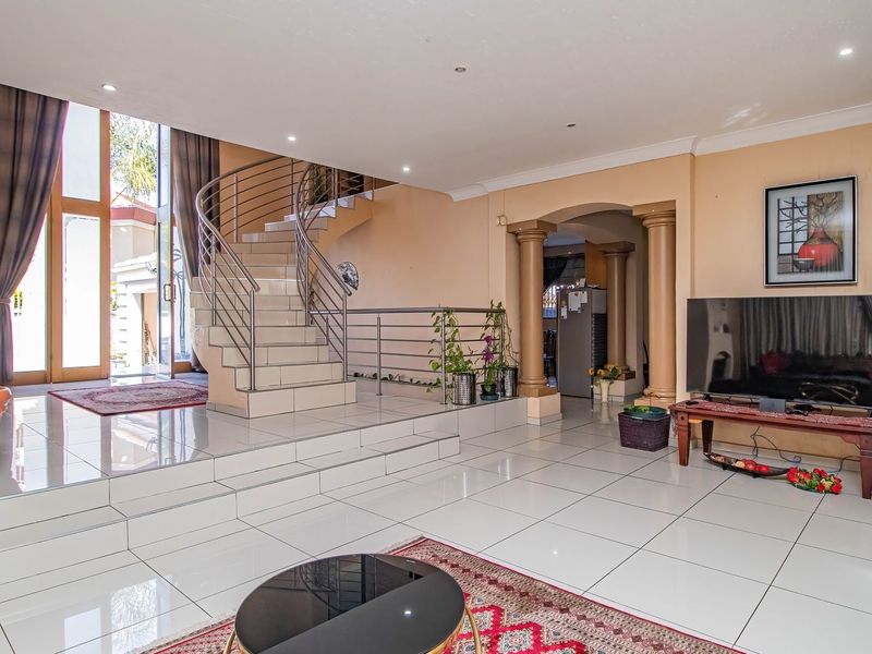Spacious living area featuring large format floor tiles, a prominent curved staircase with stainless steel balustrades, and direct access to the outdoor area.