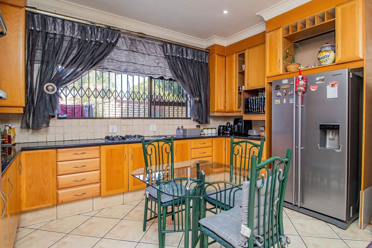 A functional kitchen featuring wooden cabinetry, granite countertops, built-in oven, gas hob, and tiled flooring, with security bars installed on the window.