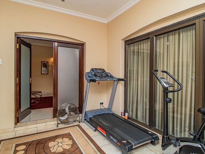 A dedicated gym space featuring tiled flooring, large sliding glass doors for natural light, and double door access to the rest of the home.