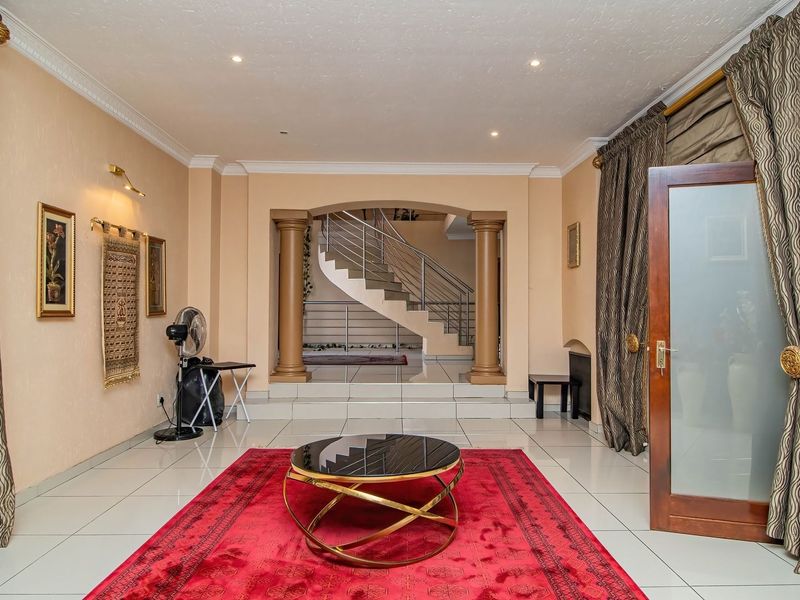 Spacious living area featuring tiled flooring, recessed lighting, and an elegant arched entryway leading to a central staircase with decorative columns.