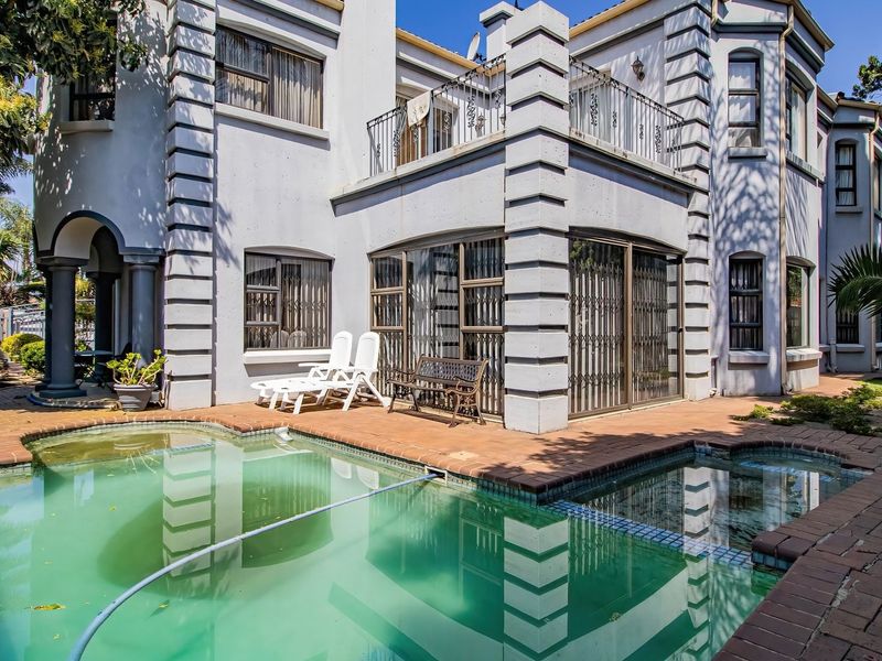 Rear exterior view featuring a swimming pool, brick patio area, and a multi-story building facade with a balcony and security features.