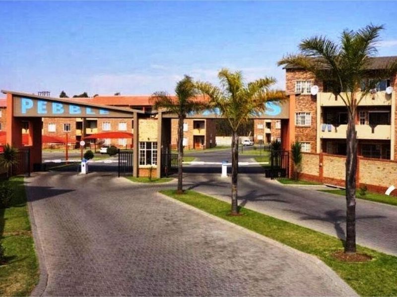 The main entrance to the apartment complex featuring a secure gatehouse, paved driveway, and established landscaping.