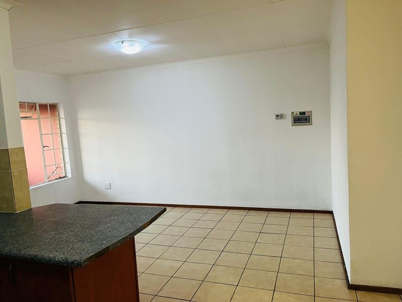 An open-plan living area featuring tiled flooring, a granite-topped breakfast counter, and secure window bars, providing a clean and functional blank canvas.