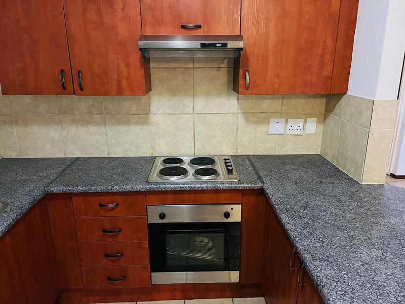 A functional kitchen featuring wooden cabinetry, granite countertops, a built-in oven, electric hob, and a tiled backsplash.
