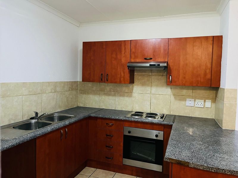 A functional kitchen featuring wood-finish cabinetry, granite-look countertops, a built-in oven, electric hob, and a stainless steel double sink with tiled backsplash.