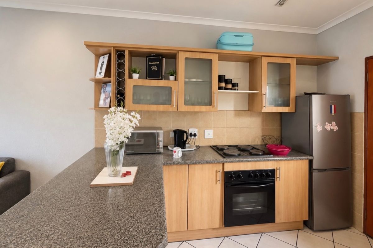 A functional kitchen featuring wooden cabinetry, granite countertops, a built-in oven, and an electric hob with a tiled backsplash.