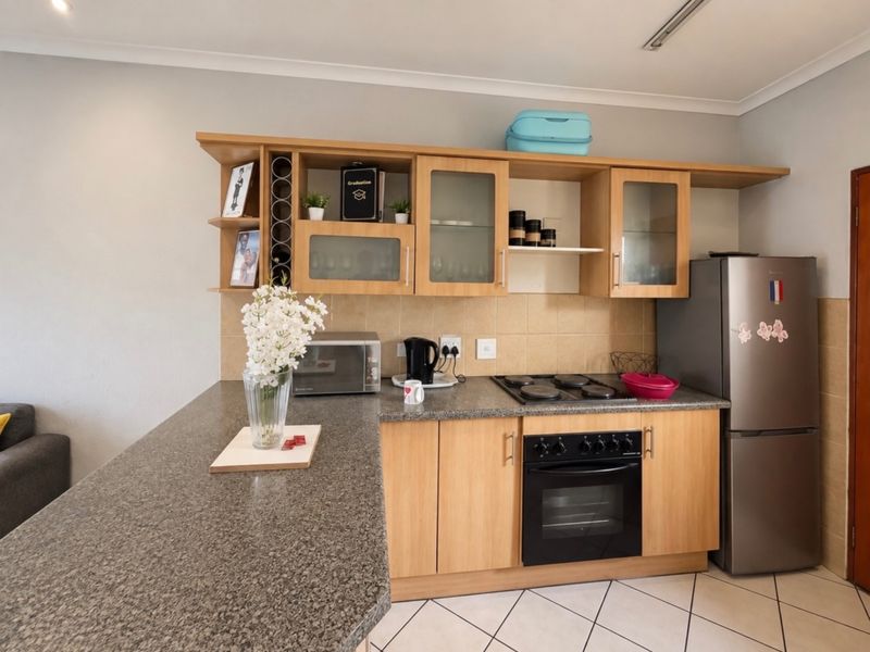 A functional kitchen featuring wooden cabinetry, granite countertops, a built-in oven, and an electric hob with a tiled backsplash.