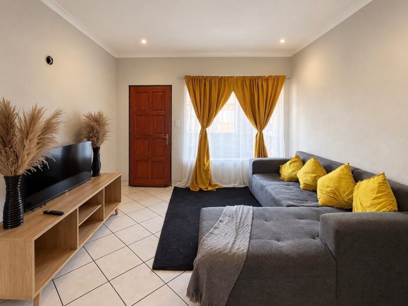 A well-maintained living room featuring neutral tiled flooring, recessed ceiling lighting, and a solid timber entrance door.