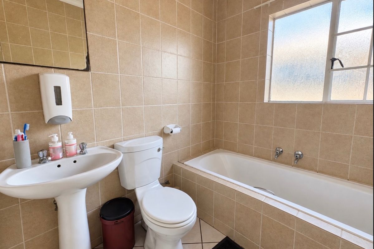 A functional bathroom featuring a pedestal basin, toilet, and a built-in bathtub with full-height wall tiling and an obscured glass window.