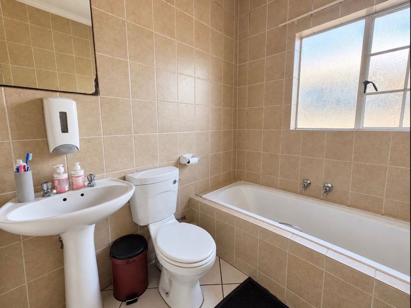A functional bathroom featuring a pedestal basin, toilet, and a built-in bathtub with full-height wall tiling and an obscured glass window.
